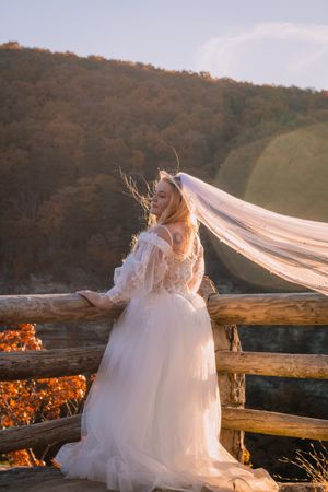 Bride's veil flows in the wind as she stands at mountain overlook during golden hour.