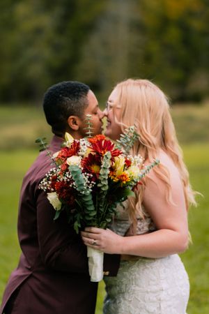 A wedding couple embraces while holding a vibrant bouquet of red and white flowers.