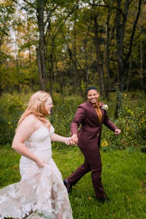 A couple dressed in wedding attire dances playfully in a lush autumn forest setting.
