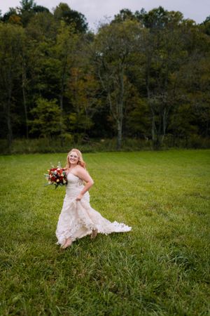 A bride in a lace gown twirls with her bouquet in a scenic meadow.