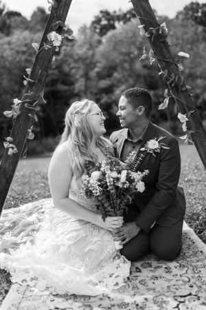A romantic black and white portrait of newlyweds under a floral arch.