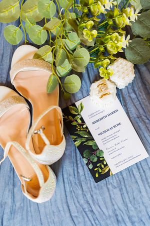 Beautiful wedding details with blush ballet flats, greenery and yellow floral accents, and an elegant invitation on blue fabric.