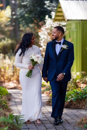 A bride and groom share a romantic moment together on a stone path surrounded by flowers in a garden setting.