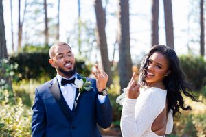 A joyful couple in wedding attire pose playfully in a sunlit forest setting.