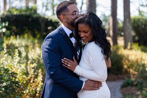 A couple in formal wedding attire share intimate moments in a sunlit outdoor garden setting.
