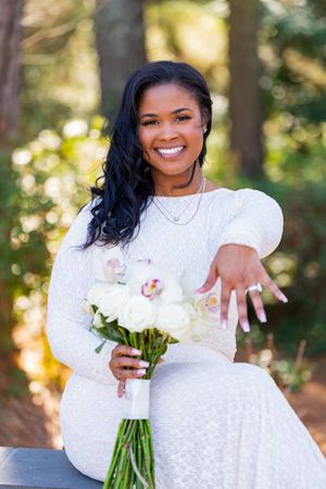 Beautiful wedding portrait outdoors showing white lace dress and bouquet of white flowers in a natural forest setting.