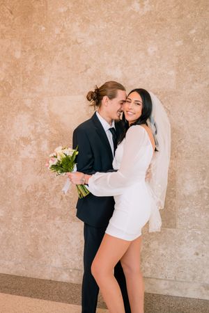 Modern wedding portraits against a textured wall with minimalist white attire.