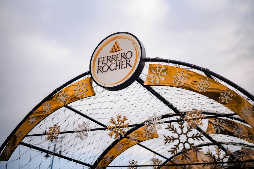 Decorative metal arch with Ferrero Rocher branding spans across a holiday market.