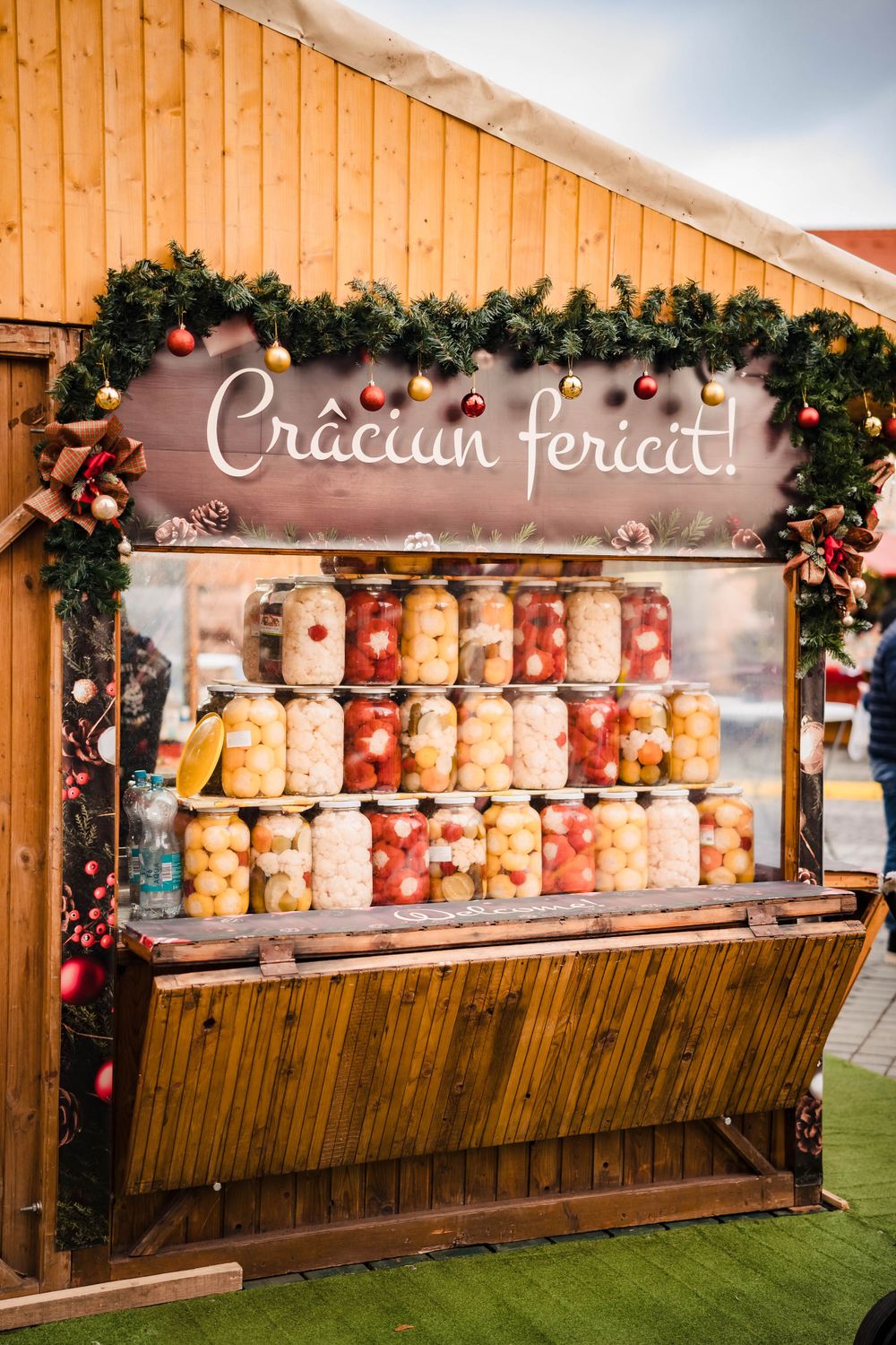 Wooden market stall displays colorful jars of preserved fruits with Christmas decorations.