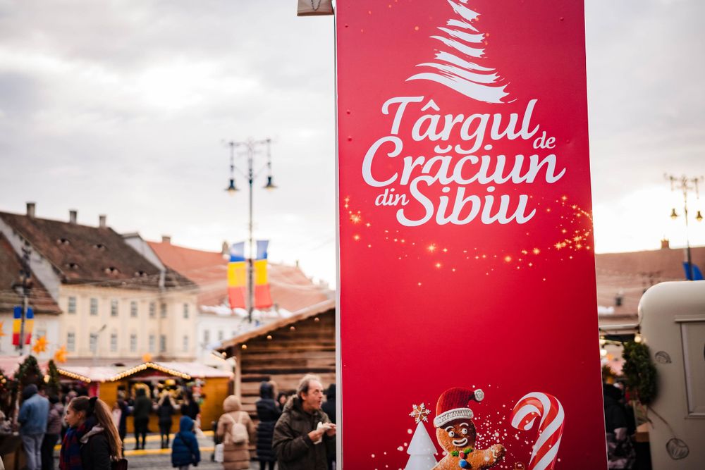 Red Christmas market banner in Sibiu with festive decorations and market stalls in the background.