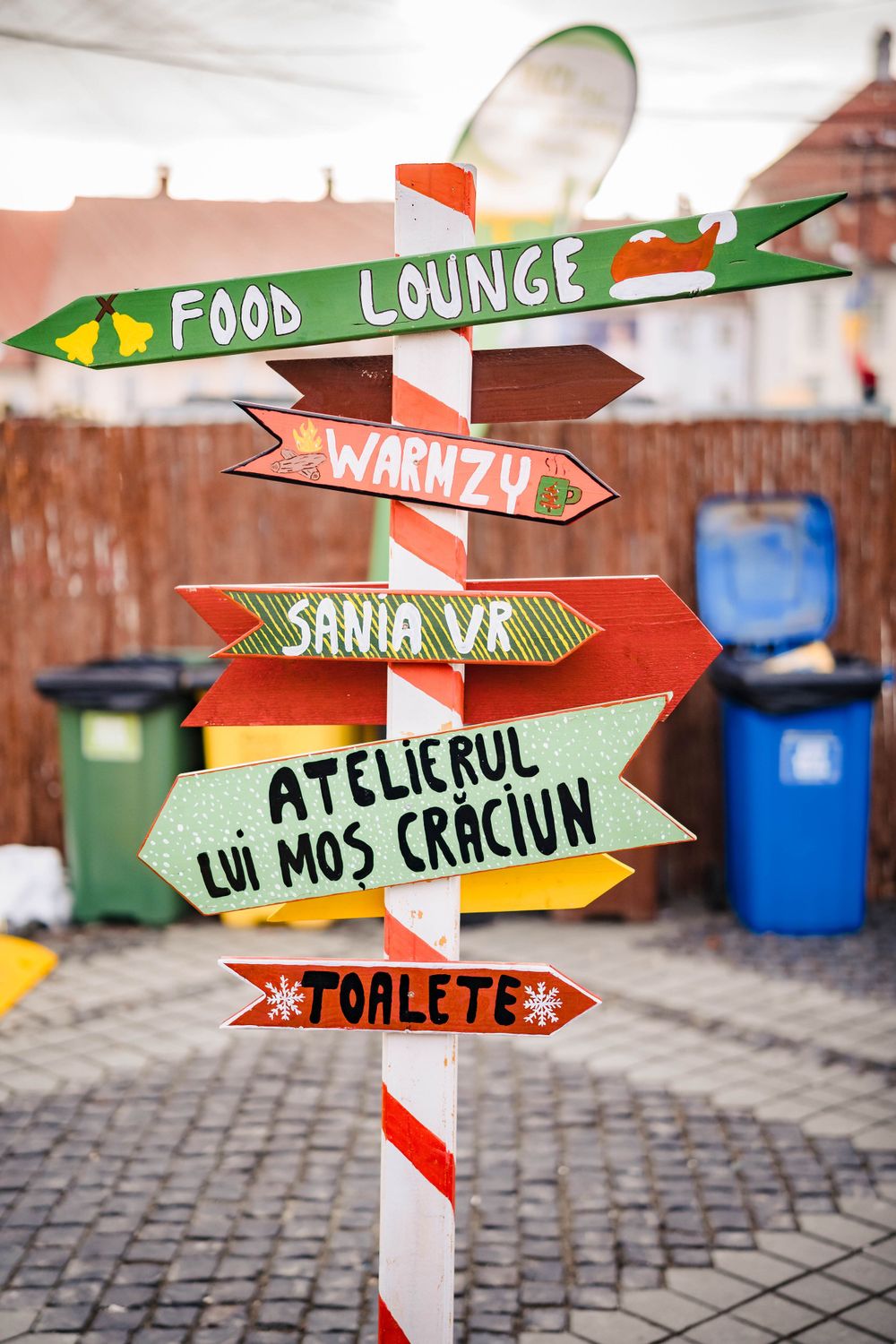Colorful directional sign post with multiple arrows pointing to food and entertainment areas at a winter market.