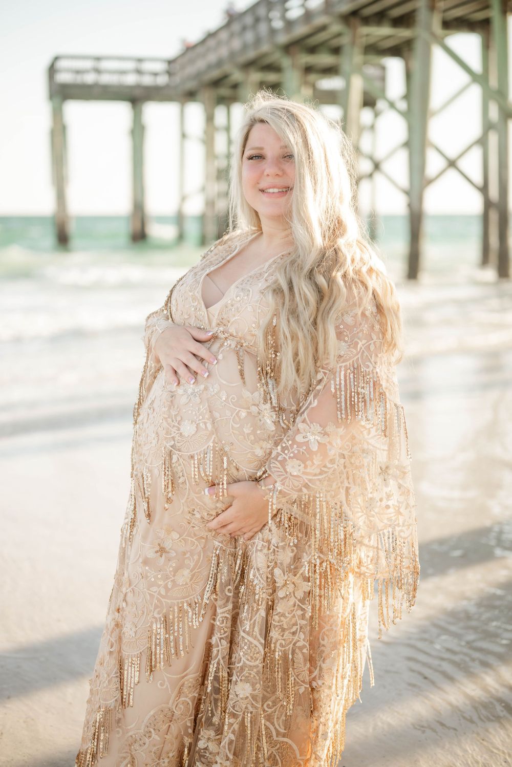 Maternity beach photo in sparkling gold dress with pier in background.