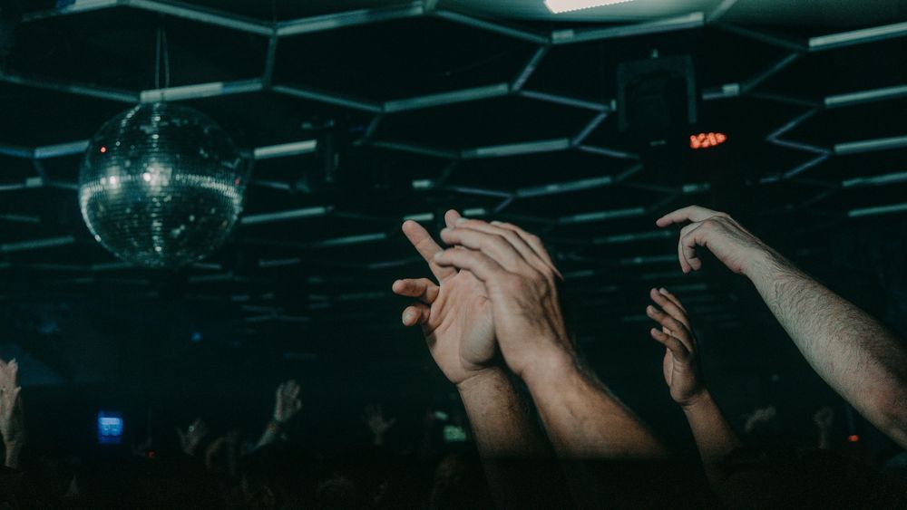 Light shining on hands raised in a club with a disco ball
