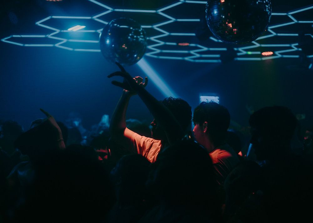 An individual dancing in a club with honeycomb ceiling lighting and disco balls