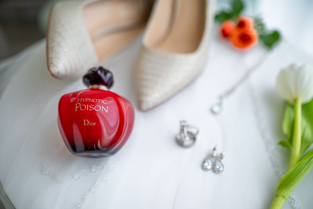 Close-up of red apple-shaped perfume bottle with bridal jewelry and white tulip.