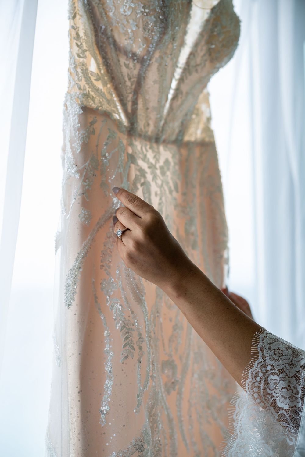 Close-up of a hand touching delicate lace detail on a wedding dress.