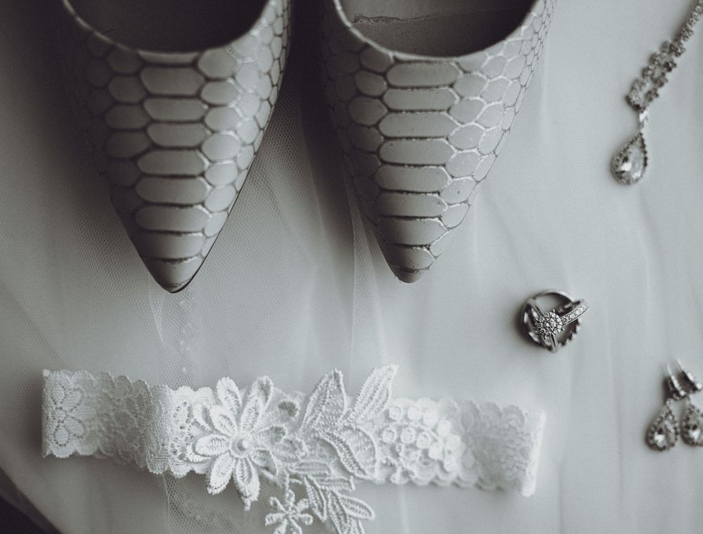Grey textured wedding shoes displayed with a delicate white lace garter and crystal jewelry accessories.