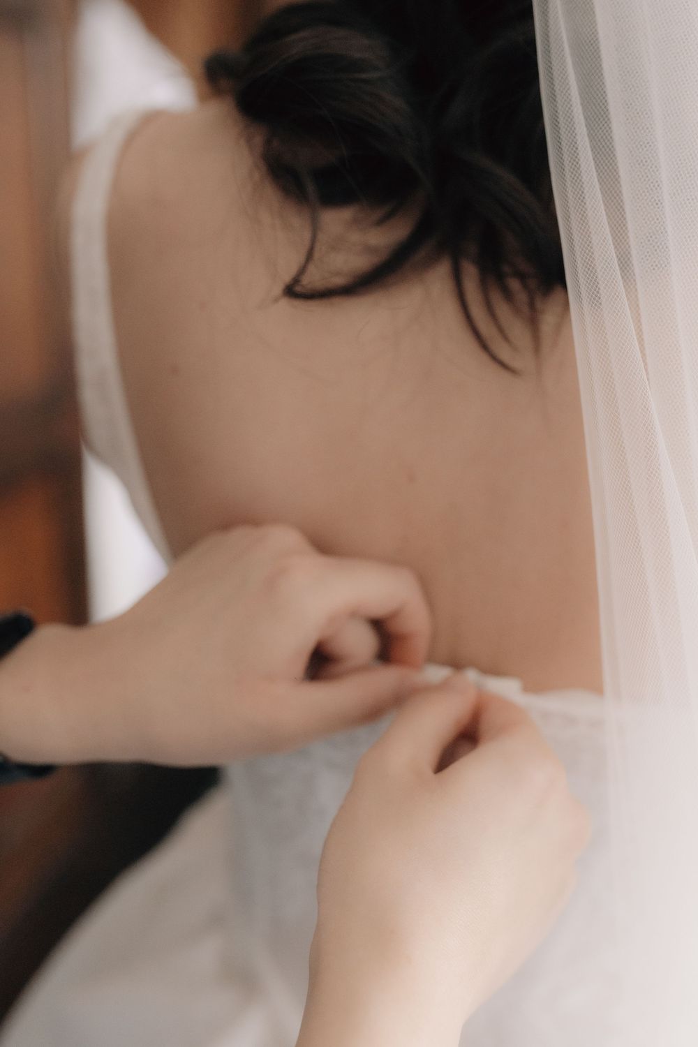 Bridesmaid carefully fastening buttons on the back of a white wedding dress.
