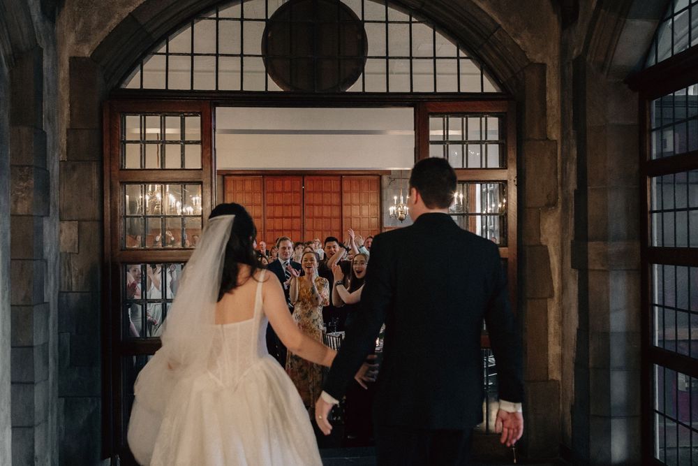 Bride and groom entering wedding reception greeted by cheering guests.
