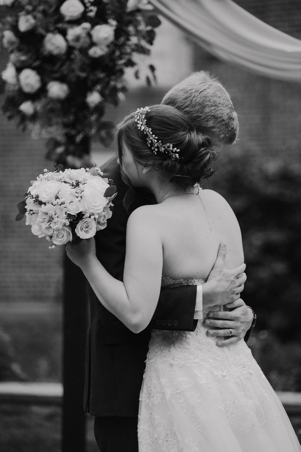 Black and white photo of bride and groom embracing at the altar, bride holding a white rose bouquet.
