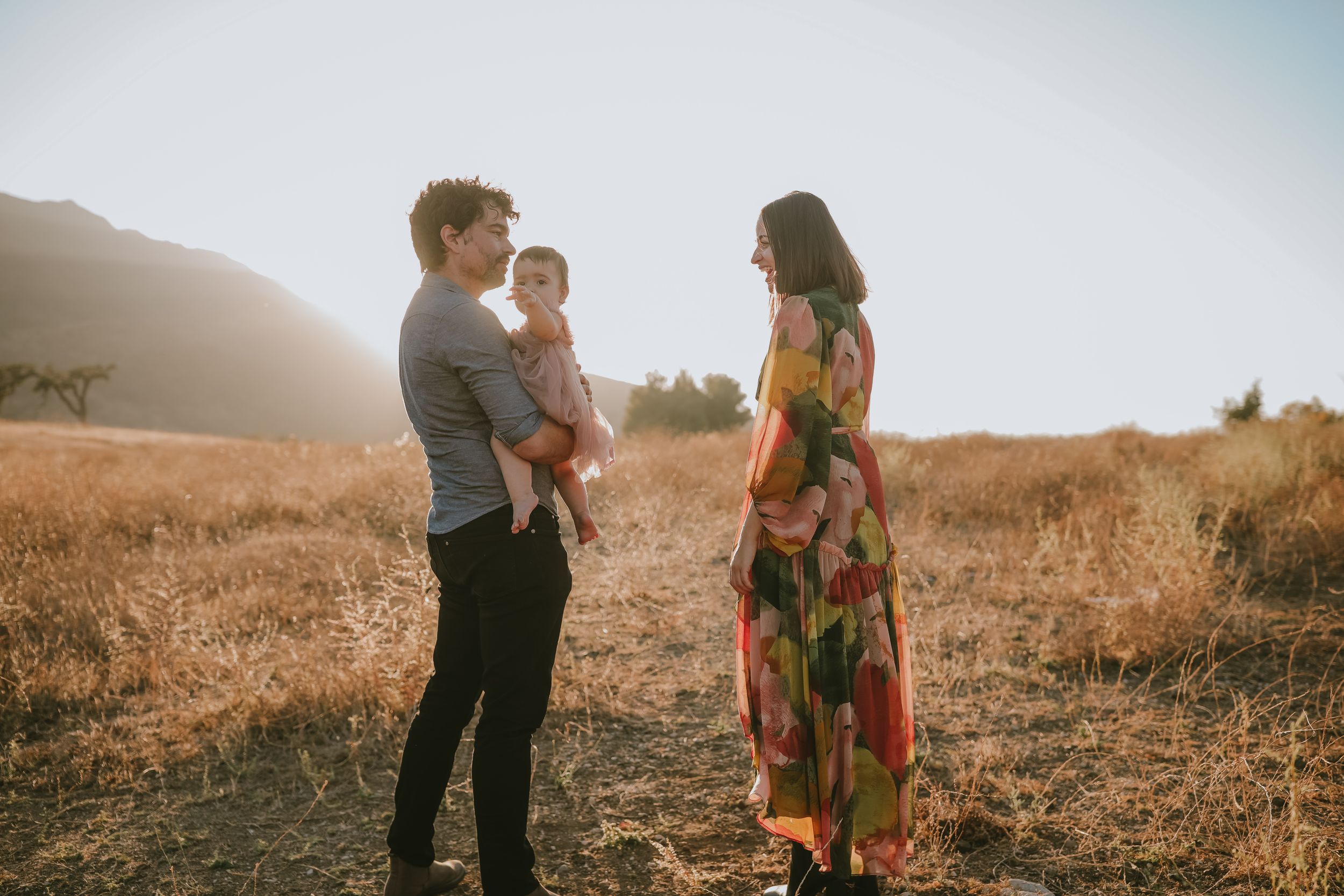 Family wearing colorful clothing stands together at sunset in a golden field on a hazy mountain afternoon.