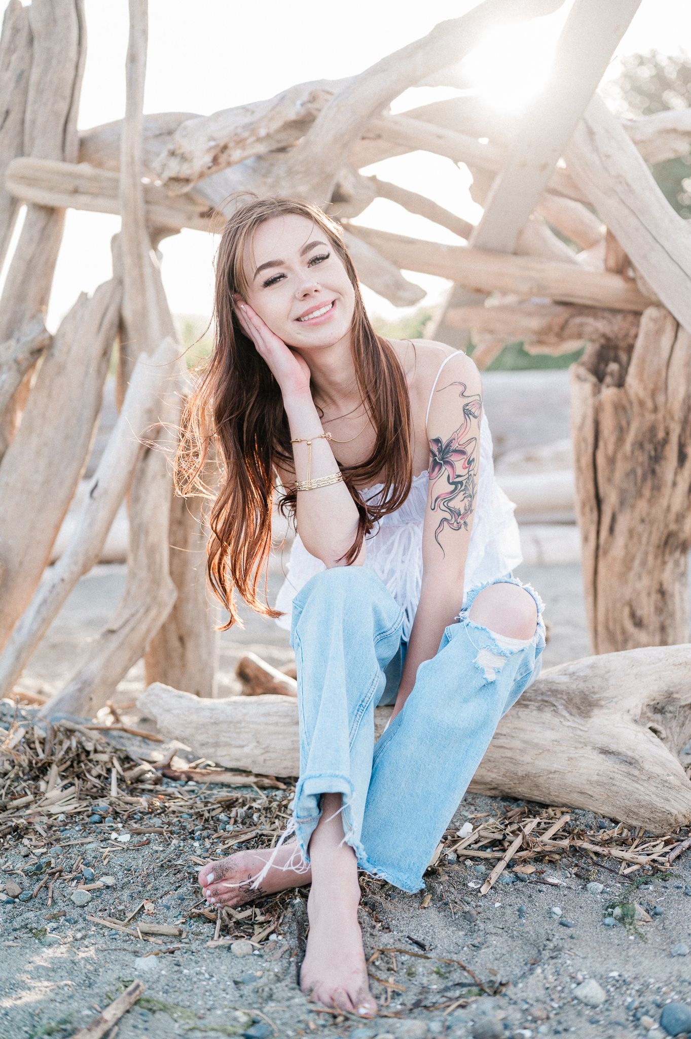 Senior girl sitting on beach in front of logs at Point No Point. Photo by Pine + Vow