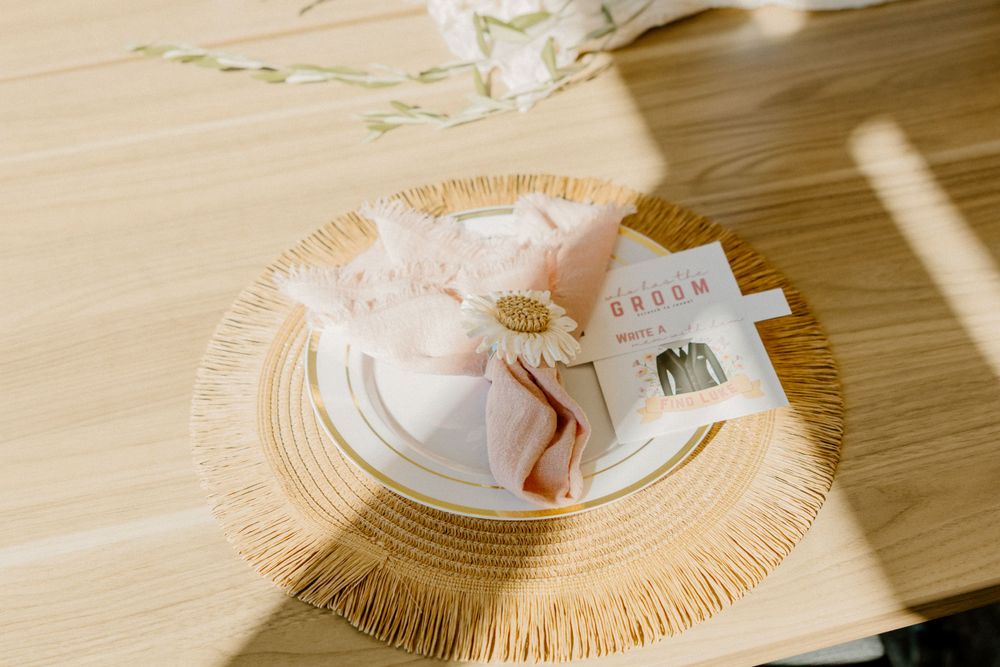 Place setting detail with natural woven charger and pink accents in sunlit room.