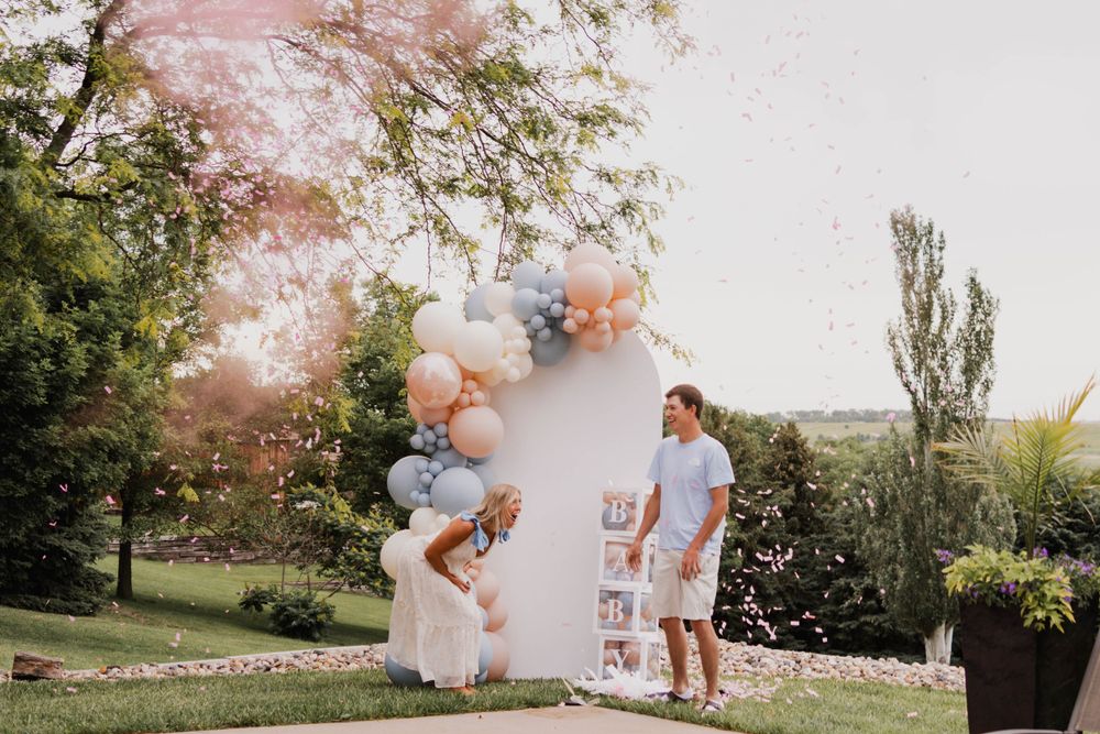 Outdoor celebration space with balloon arch and decorative elements in pink and white.