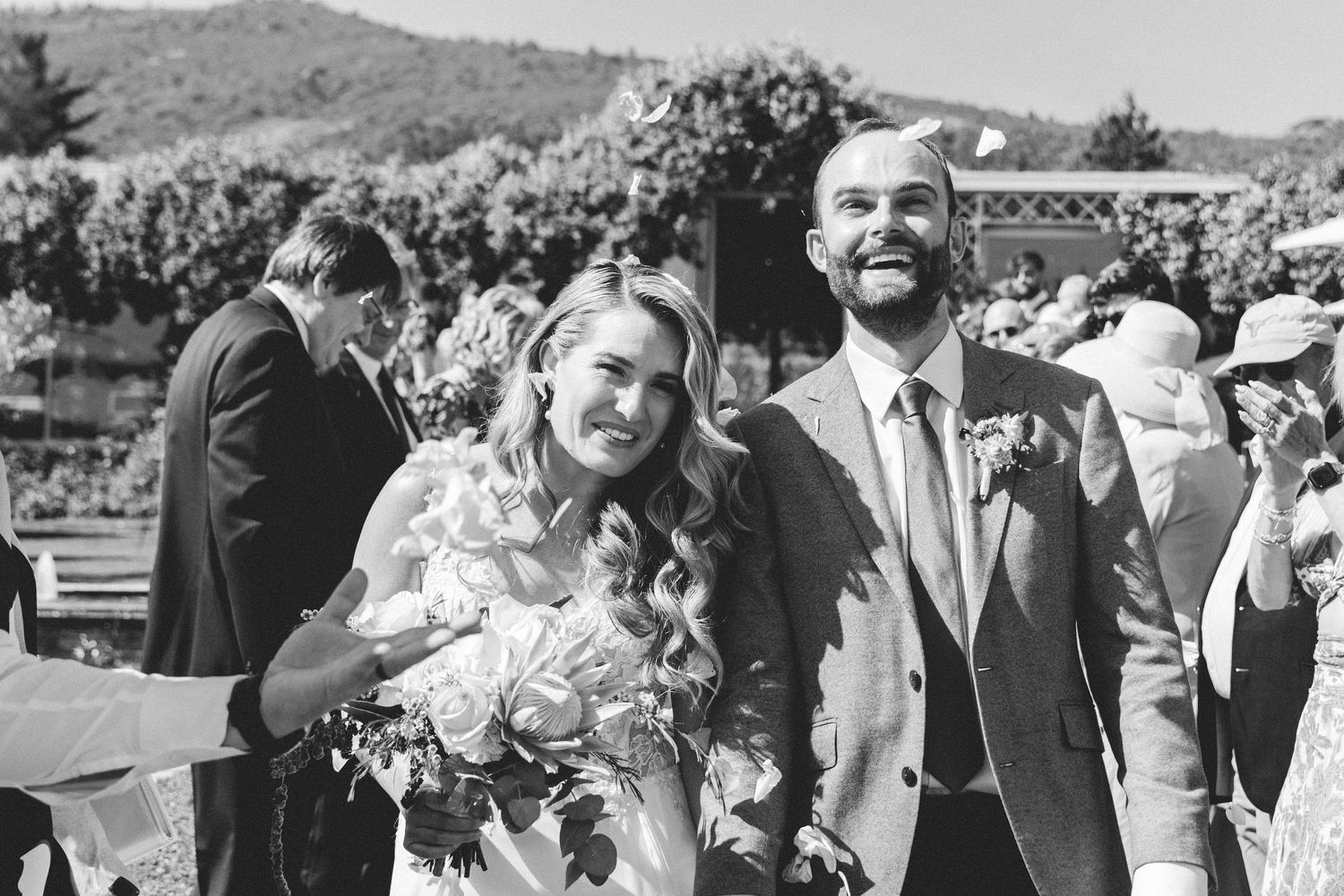 Wedding couple celebrates outdoors with guests in a scenic garden setting.