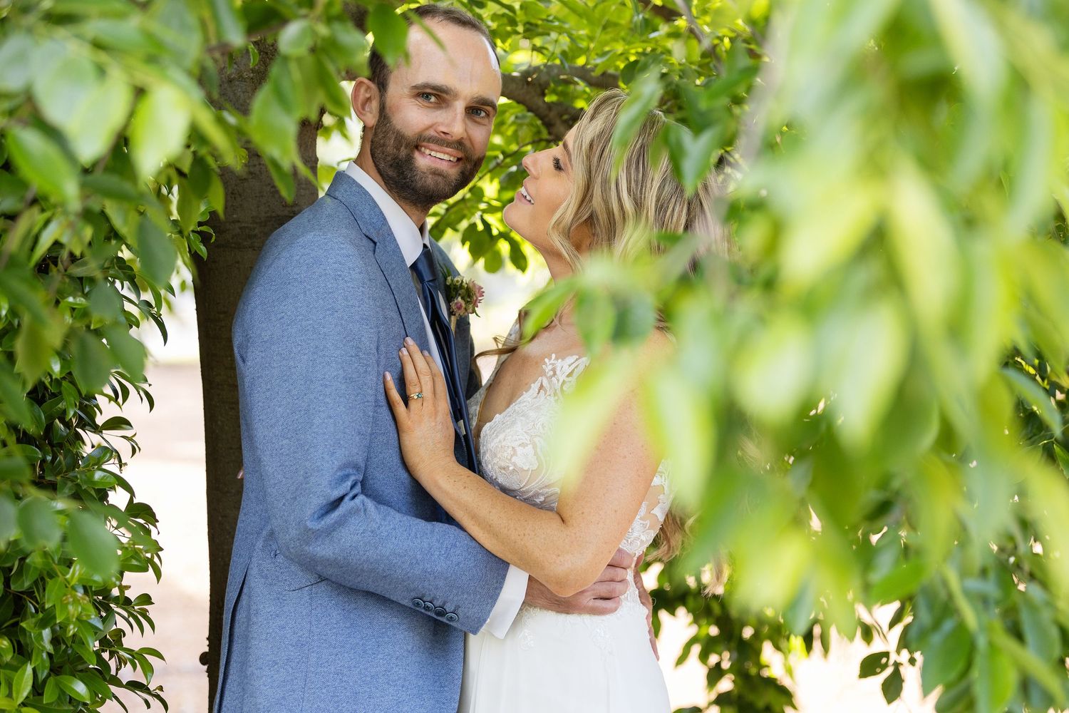 Intimate moment between newlyweds surrounded by lush green foliage.