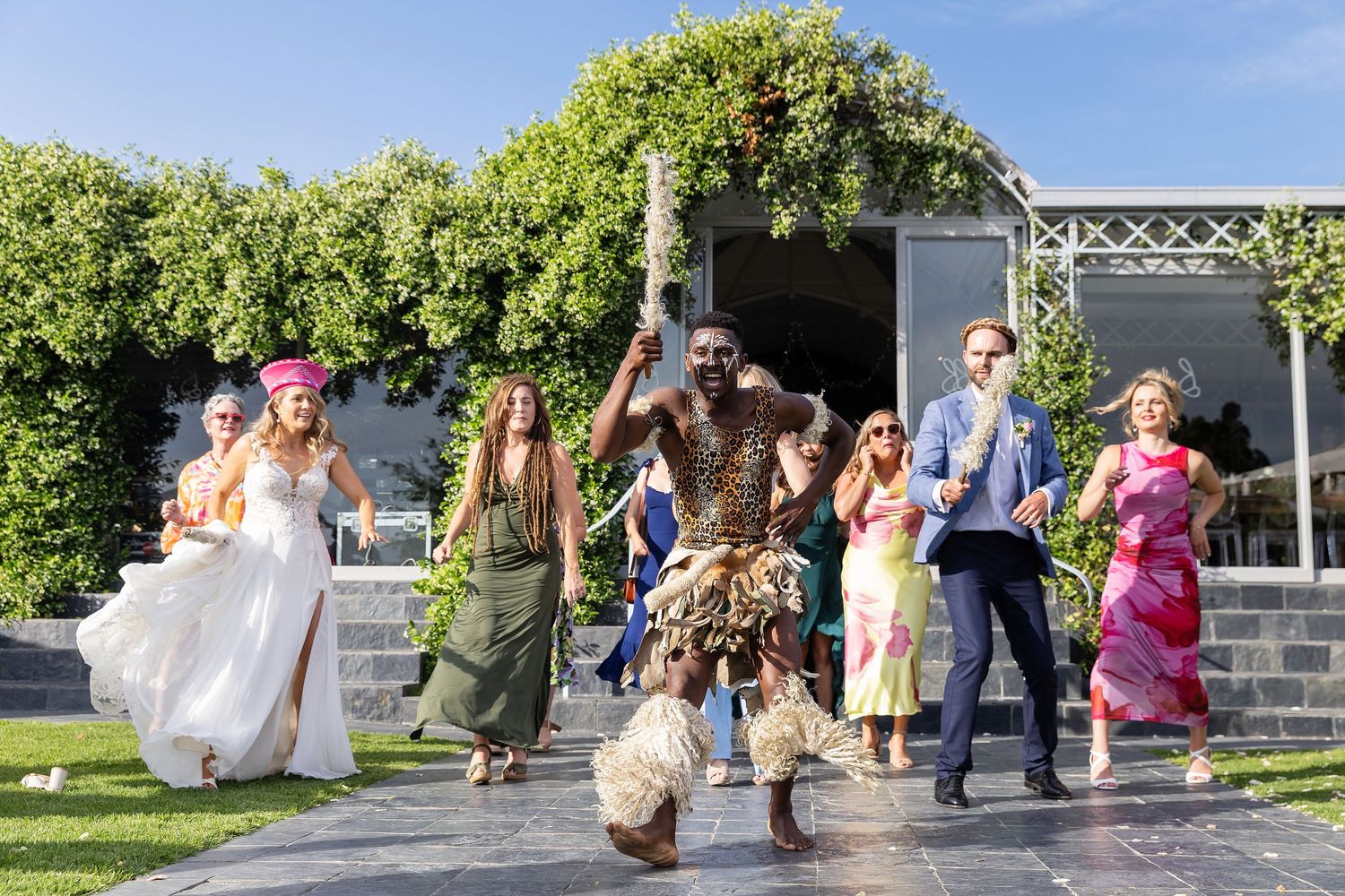 Wedding party jumps joyfully on garden steps during celebration.