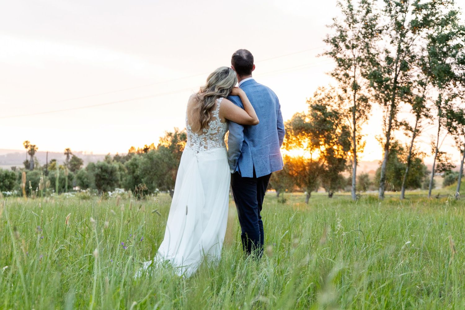 Couple embraces while watching sunset in a serene meadow.