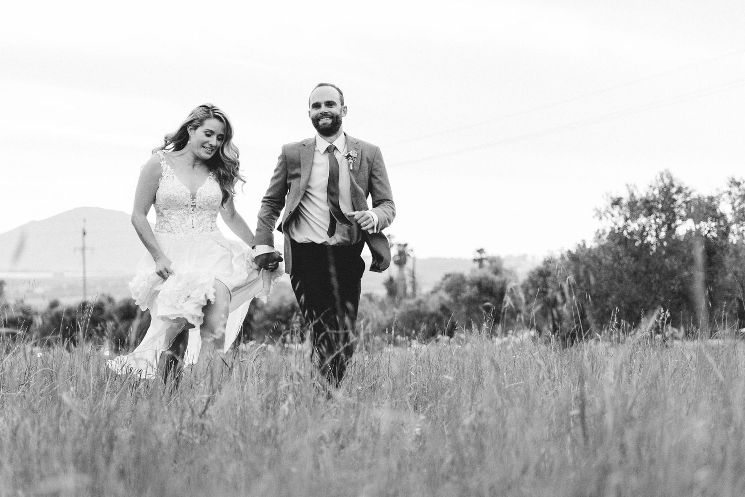 Couple runs playfully through a meadow of tall grass in black and white.