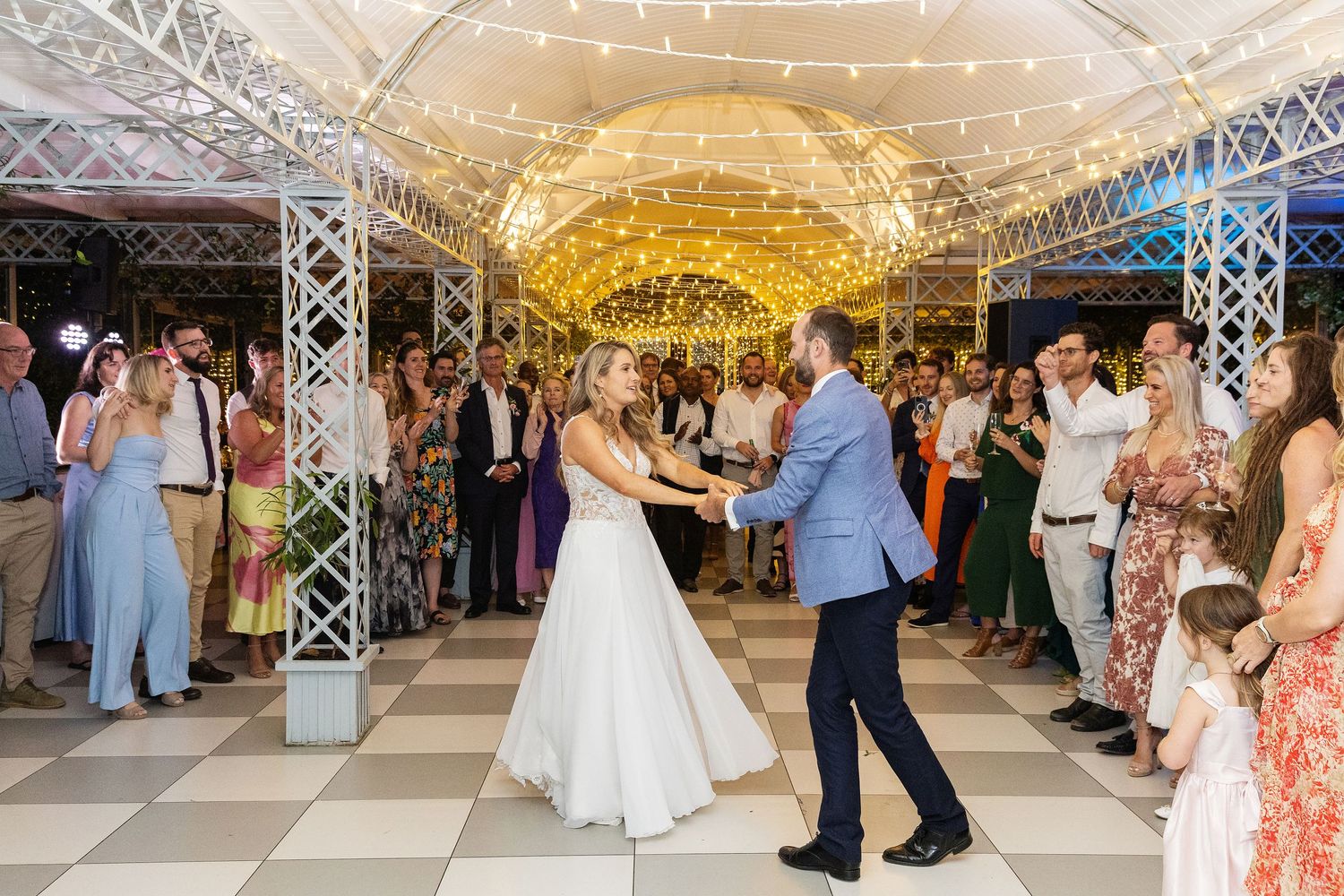 Newlyweds share their first dance under twinkling lights at elegant reception venue.