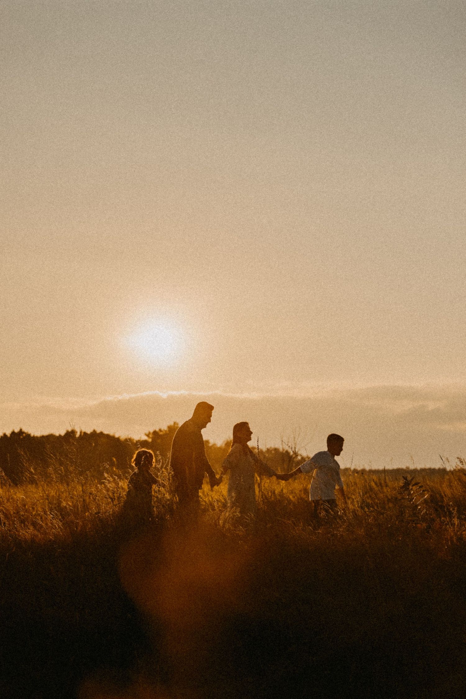 Silhouettes of family walking together against setting sun in field.