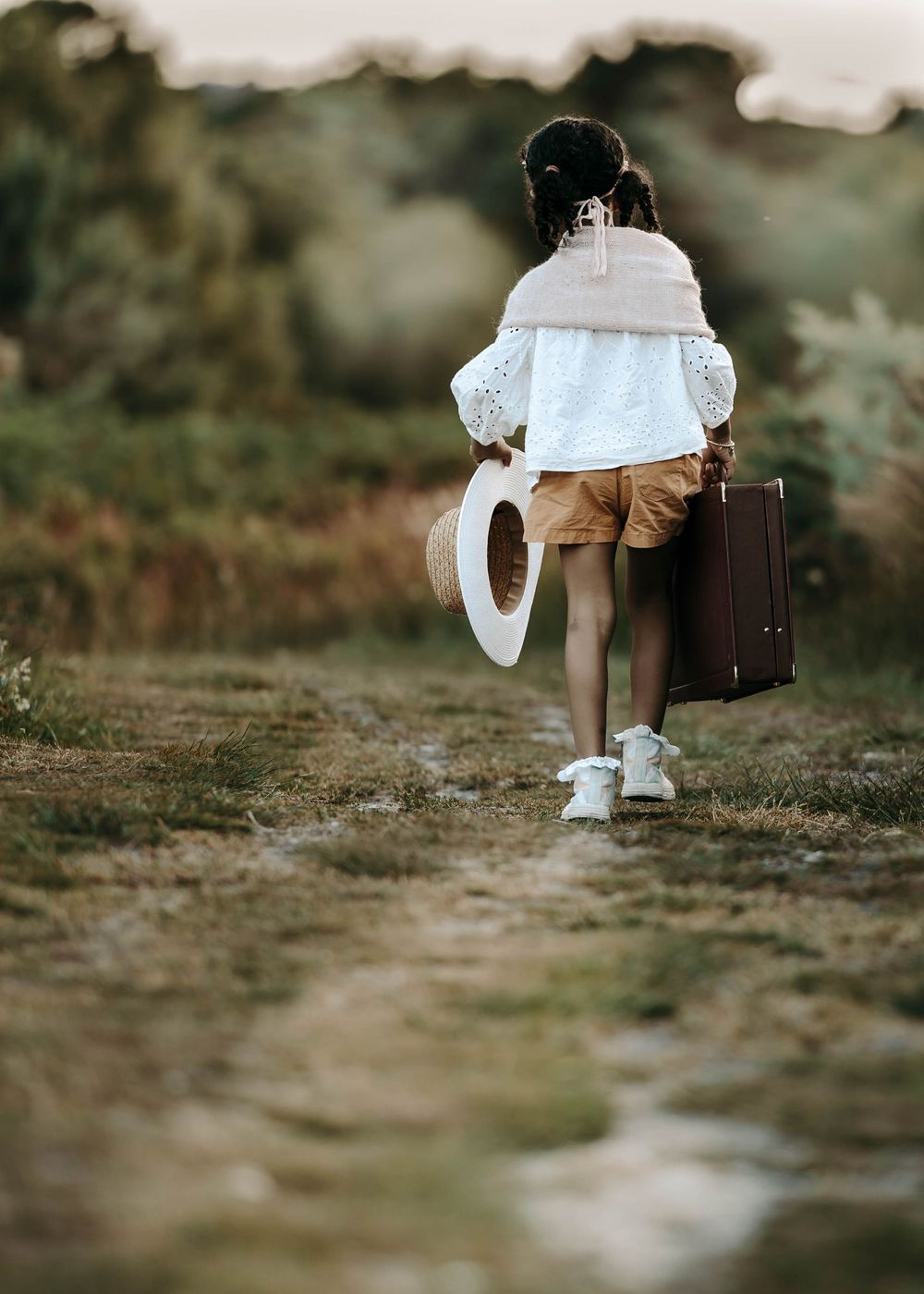 A person walking down a path carrying a suitcase and ring light in warm evening light.