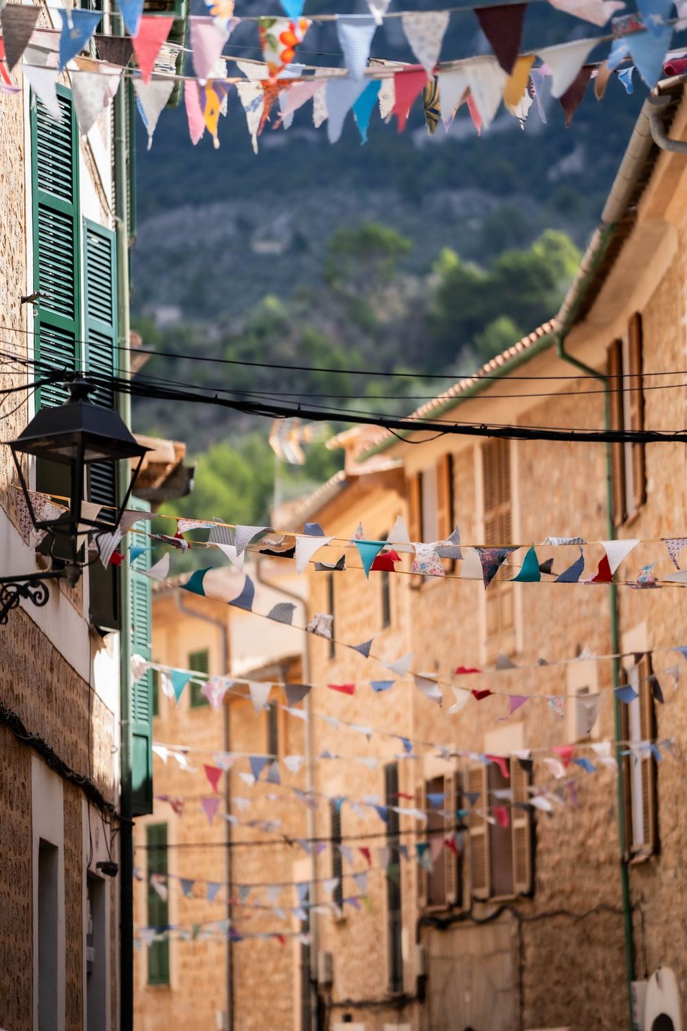 Colorful triangle bunting flags strung across a narrow Mediterranean street with traditional buildings.