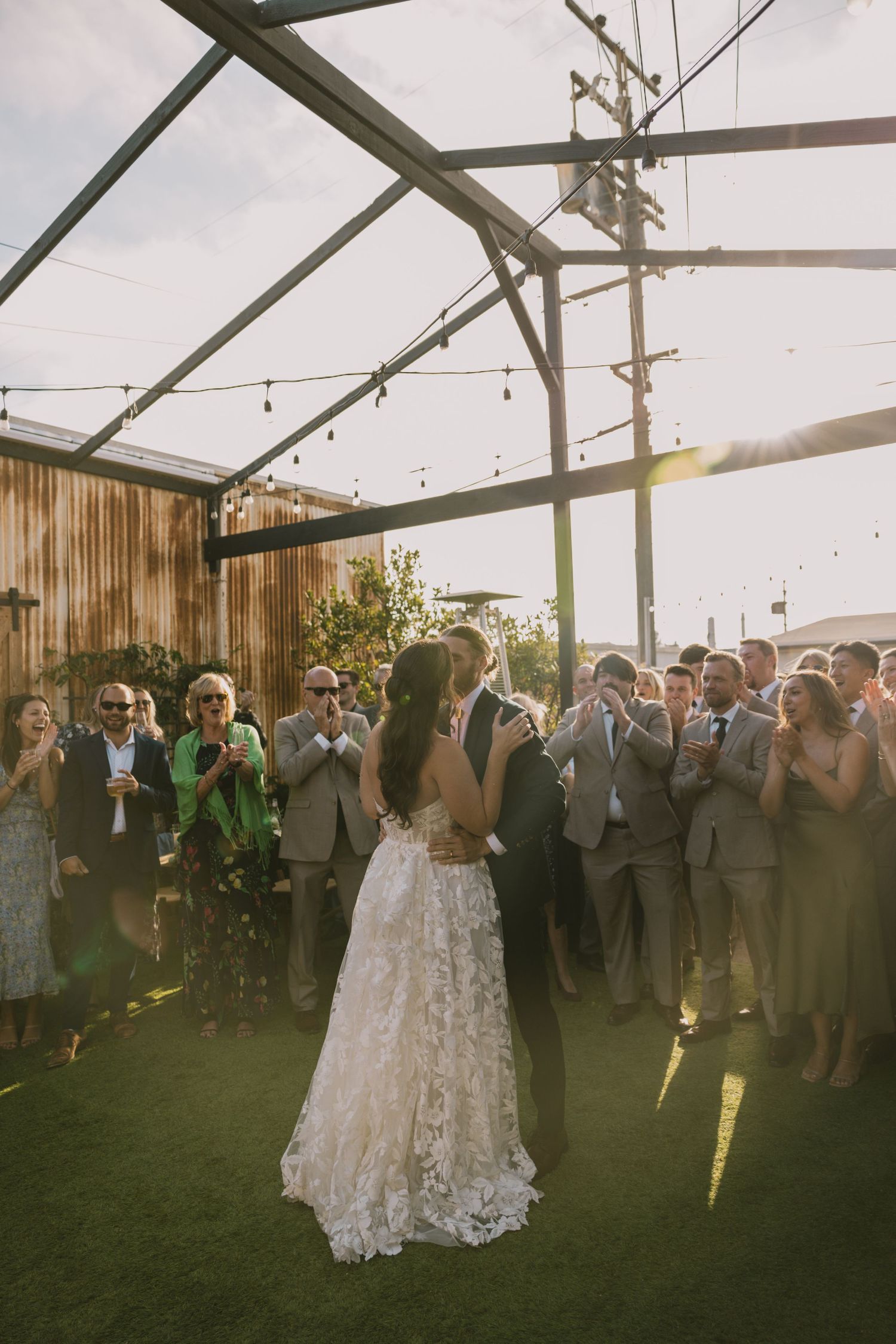 Wedding celebration under a transparent tent with string lights at sunset.