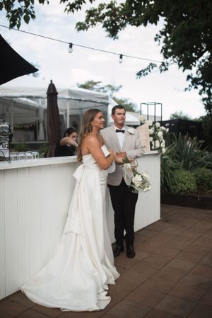 Couple dances together on outdoor patio with white fence and string lights.