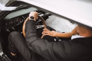 Close up view of hands on steering wheel in vintage car on wedding day.