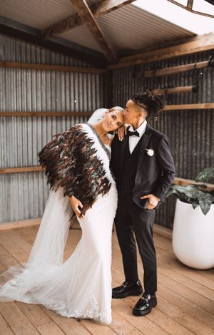 Couple shares romantic moment in rustic venue with bride wearing feathered shawl.