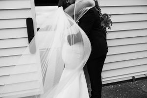 Artistic black and white photo of a couple embracing against white siding at a wedding.