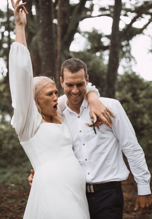 Joyful candid moment between couple in white attire outdoors.
