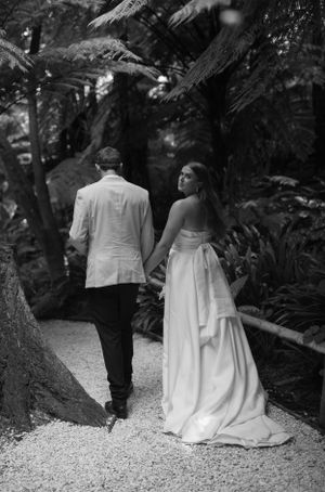 Black and white photo of a couple walking down a gravel path surrounded by lush gardens.