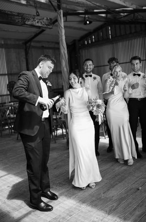 Black and white photo of wedding party dancing and celebrating in rustic venue.