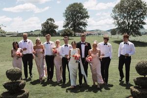 Wedding party in pink and white attire posing outdoors on sunny summer day.