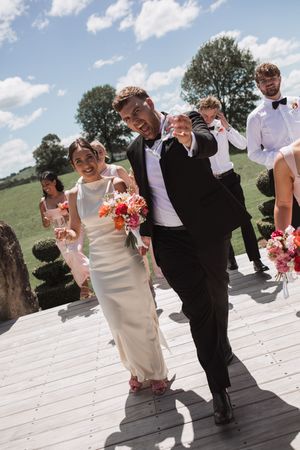 Joyful wedding party walking together on white deck during outdoor celebration.