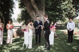 Outdoor wedding ceremony setup with white chairs arranged in rows beneath tall trees.