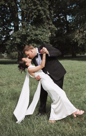 Romantic wedding couple posing for dramatic dip kiss photos on green lawn.