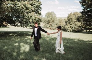 Newlyweds share playful moments during outdoor wedding photo session in a grassy field.